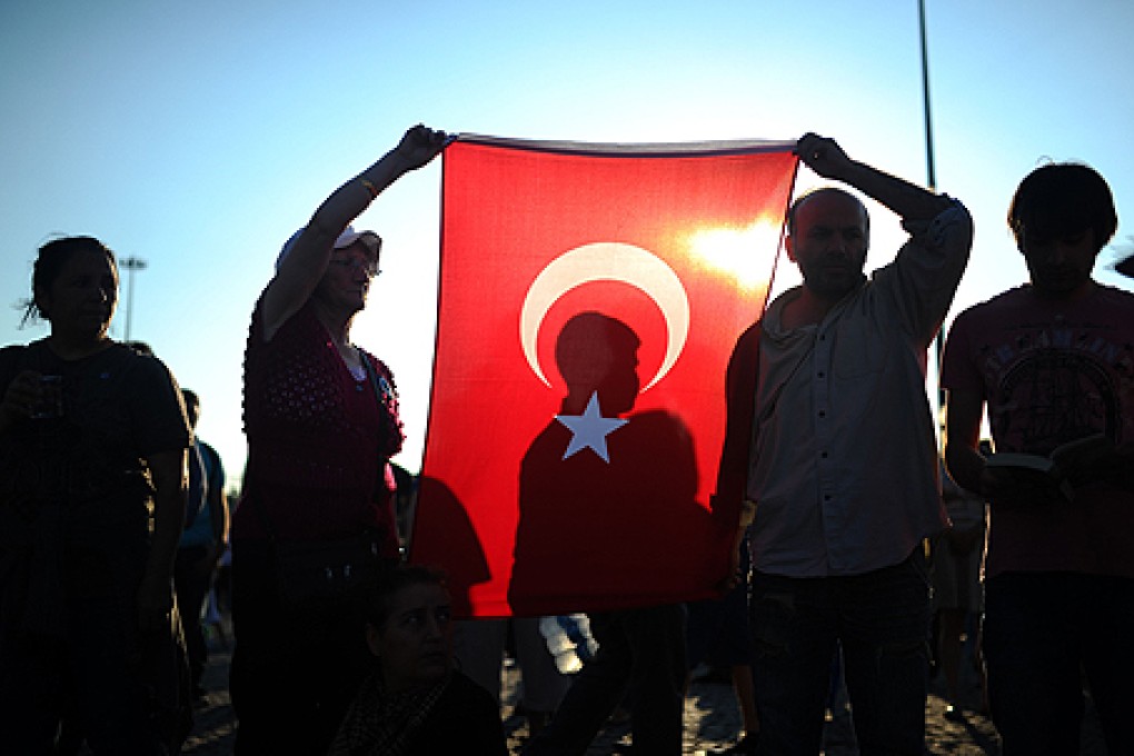 People hold a Turkish national flag as they stand on the flashpoint Taksim square in Istanbul on June 18. Photo: AFP