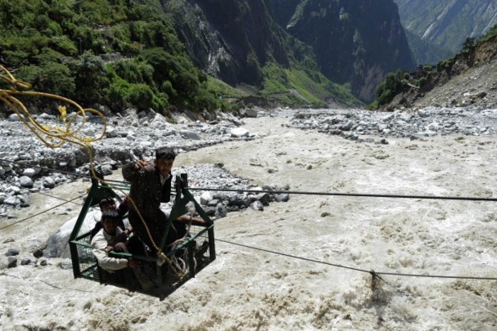 A local man throws a rope as he and others riding a gondola cross the Alaknanda river from the Hemkund Sikh temple to Govindghat following flash floods in Uttarkhand state. Photo: AFP