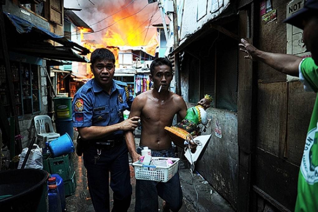 A policeman leads away a slum resident who managed to salvage a few belongings from his burning house yesterday. Photo: AFP