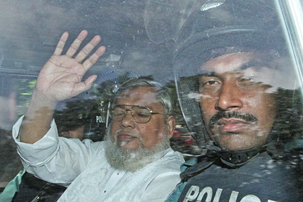 Secretary General of Jamaat e Islam, Ali Ahsan Mohammad Mujahid (left) waves from a police vehicle as he is transported to the central jail following his court verdict in Dhaka on Wednesday. Photo: AFP
