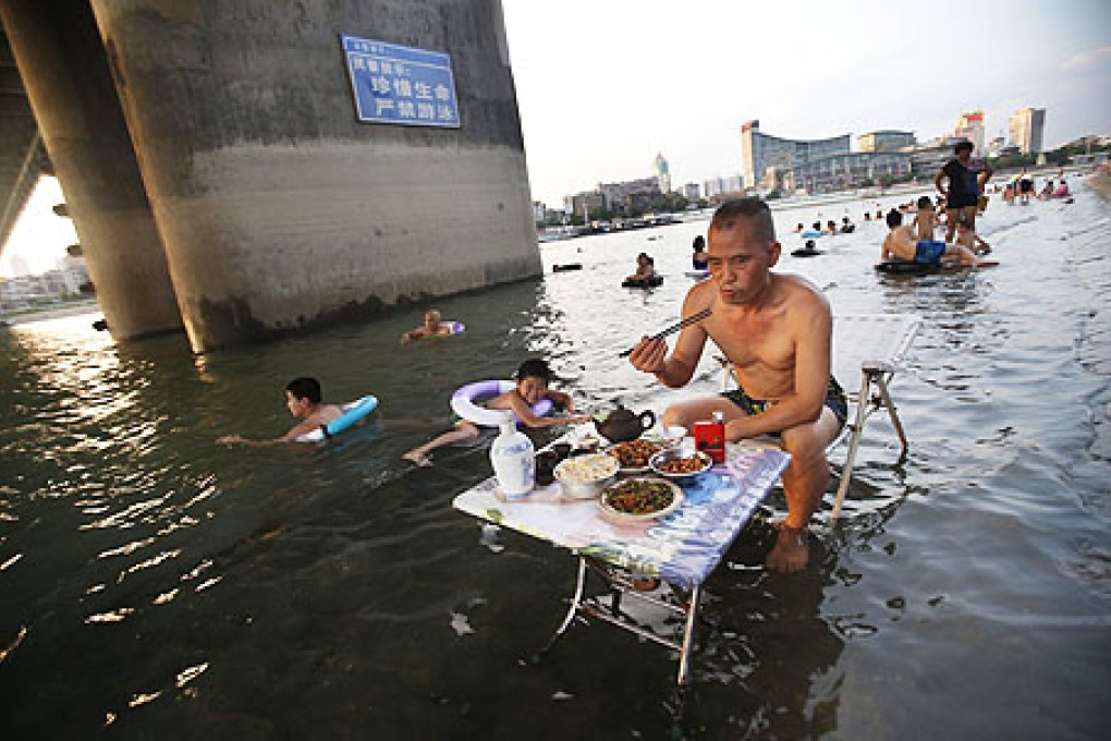 A man eats while children cool off in the Hanjiang River in Wuhan in central China's Hubei province on Sunday. Photo: EPA