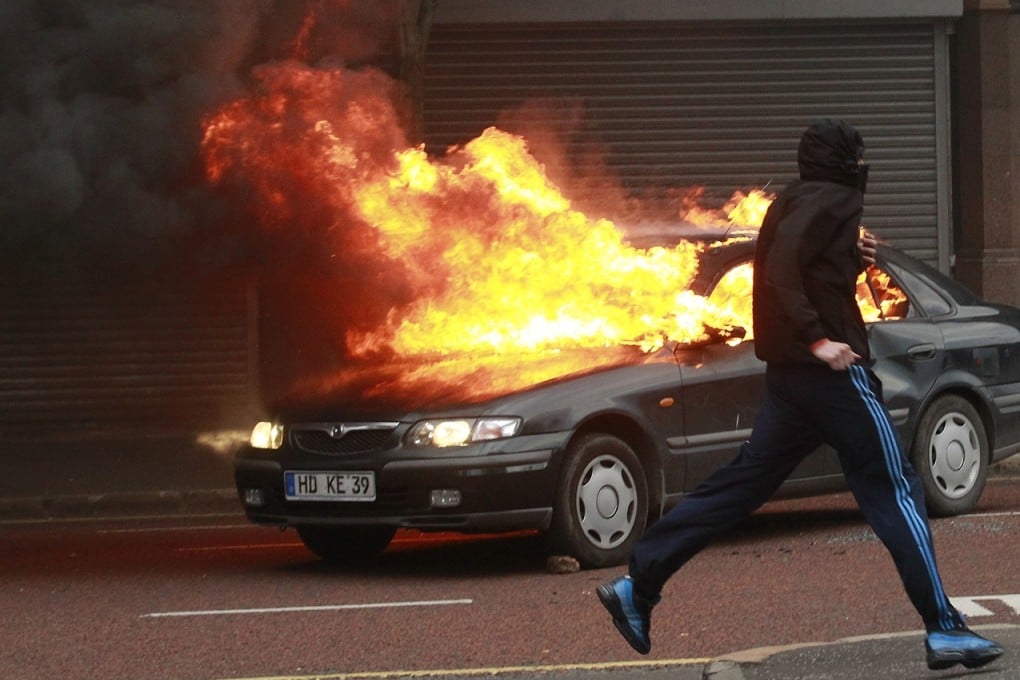 A Loyalist protester runs past a burning car during rioting in the centre of Belfast on Northern Ireland, Friday. Photo: AP