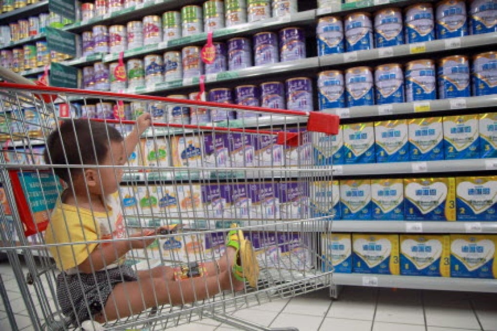 A baby stays in a shopping cart as his mother selects baby milk in a supermarket. Chinese mothers have signalled a continuing preference for foreign brands even after the Fonterra scandal. Photo: AFP