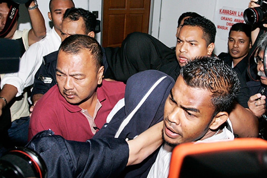 Former policemen Azilah Hadri (centre covered with blue cloth) and Sirul Azhar Umar (back centre covered with black cloth) are escorted by police as they leave a court in Shah Alam, outside Kuala Lumpur, Malaysia. Photo: AP