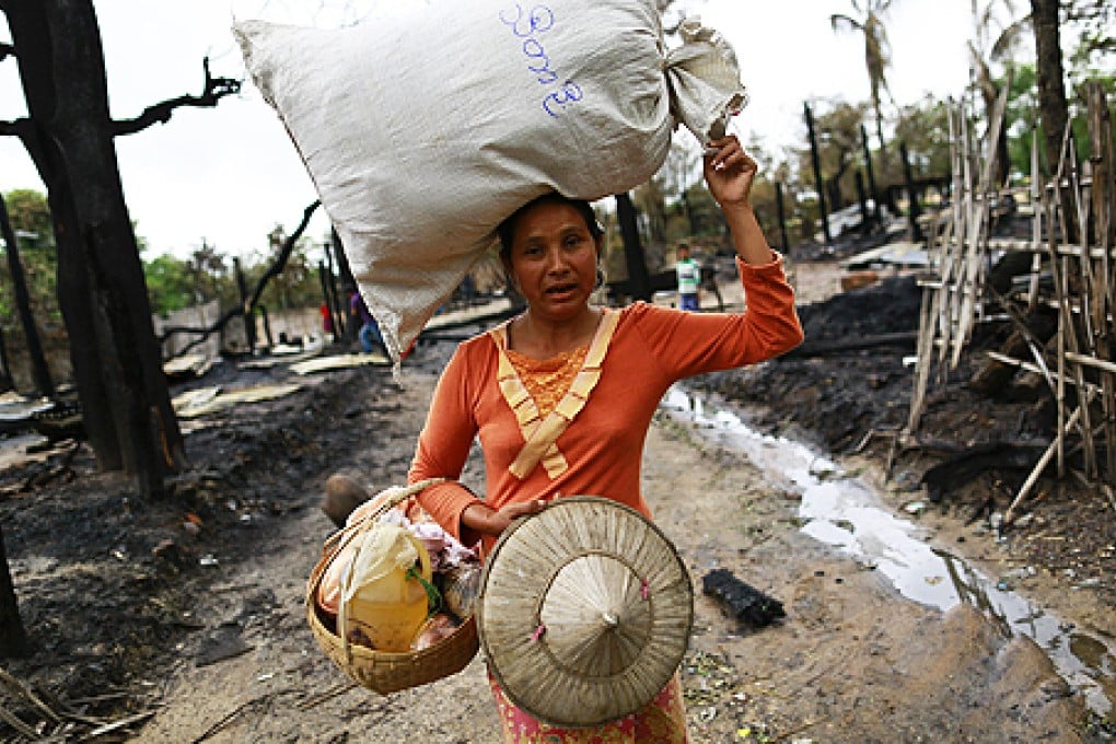 A woman carries a sack on her head as she walks past burnt houses at Htan Kone village, in Myanmar's northern Sagaing region on Monday. Photo: Reuters