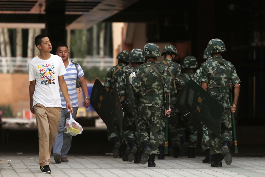 Residents walk past as armed paramilitary policemen patrol along a street in Kashgar last month. Photo: Reuters