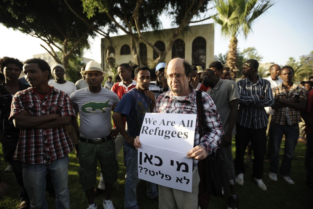 An protester in Tel Aviv stands next to African migrants holding a slogan condemning Israel's policy towards African migrants. Israel plans to deport migrants from Eritrea and Sudan. Photo: AFP
