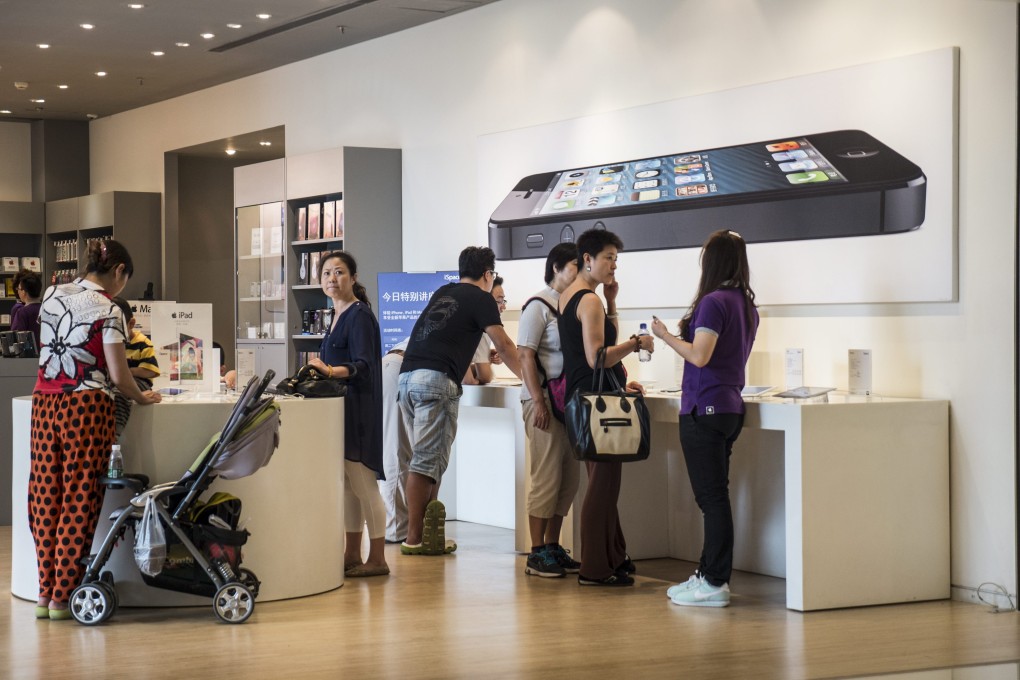 Customers look at devices on offer beneath a poster of an iPhone 5 smartphone at an Apple retailer in Beijing. Photo: EPA