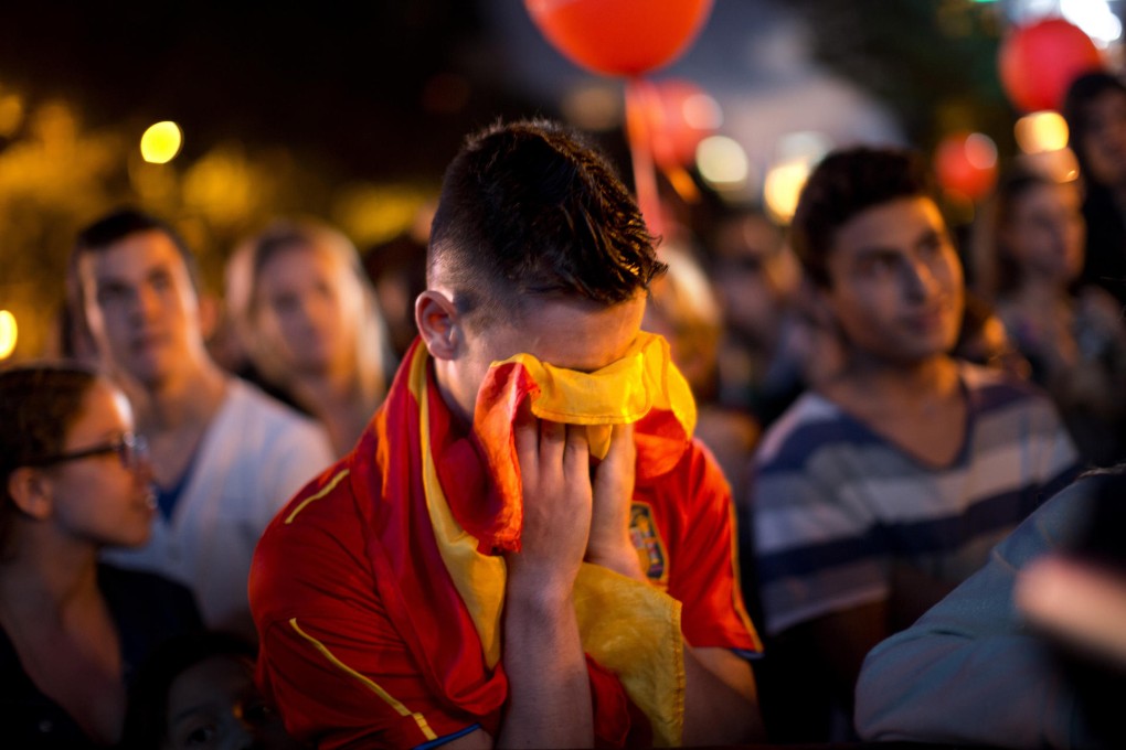 A downcast Spaniard covers his face with a flag in Madrid. Photo: AP