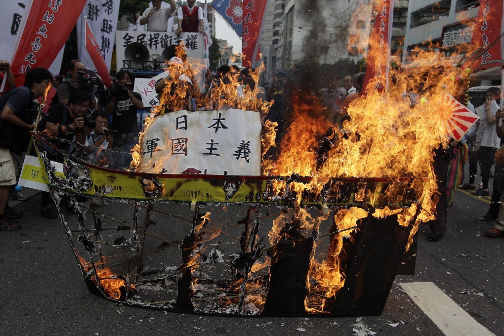 Activists burn a paper ship symbolising Japan's helicopter destroyer Izumo during an anti-Japan protest in front of the Japan Interchange Association in Taipei