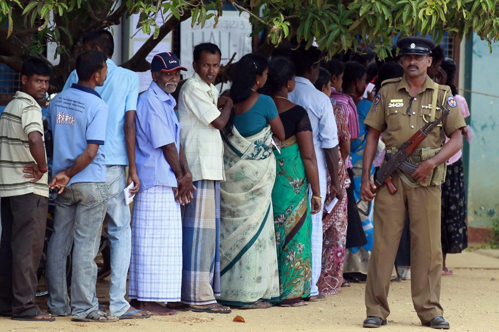 An armed police officer watches over ethnic Tamil voters in the war-ravaged north as they wait to vote on forming their first functioning provincial government. Photo: AP