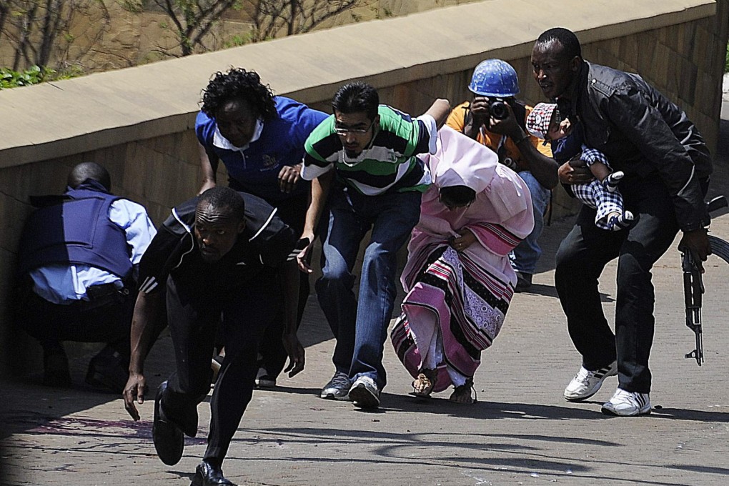 A policeman carries a baby to safety as shoppers flee. Police were going shop to shop to evacuate terrified people. Photo: AFP