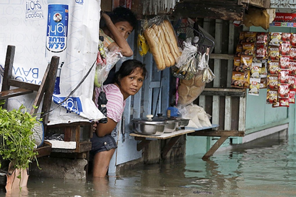 A shopkeeper looks out from her store amidst flooding at suburban Quezon city, northeast of Manila on Monday. Photo: AP
