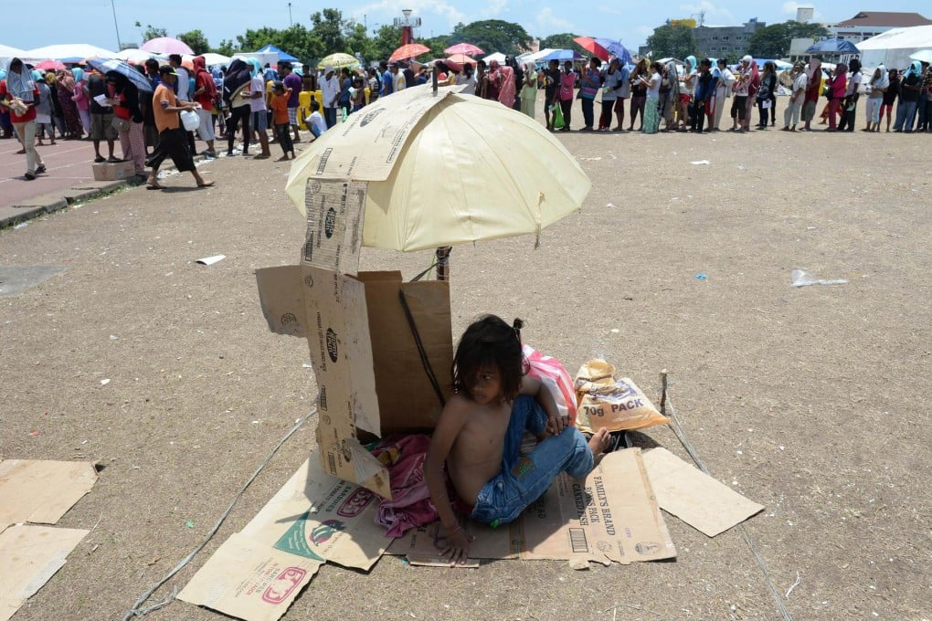 An evacuee from the stand-off between troops and Muslim rebels takes shelter from heat while others wait for food. Photo: AFP