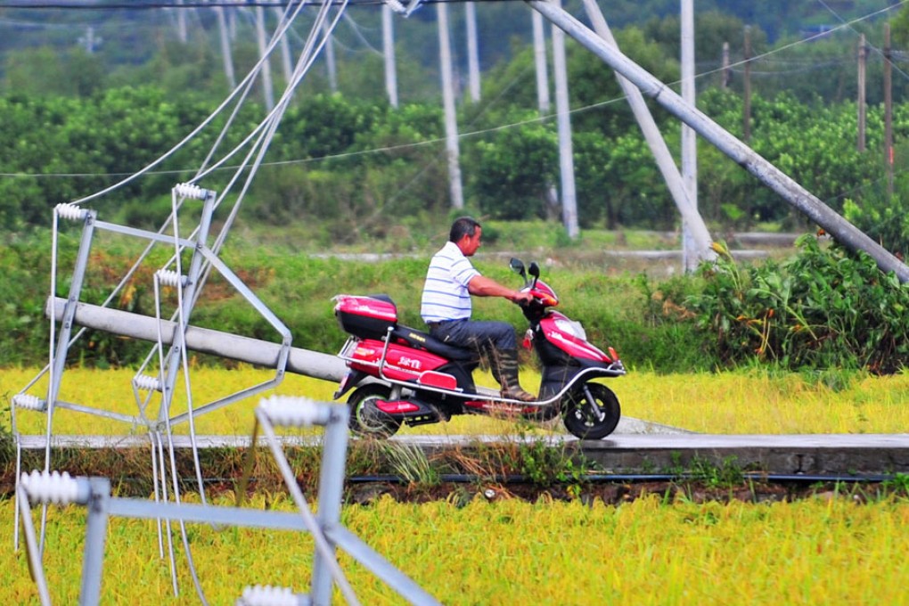 A villager rides past utility towers brought down by high winds in Fuding city, Fujian. Photo: Xinhua
