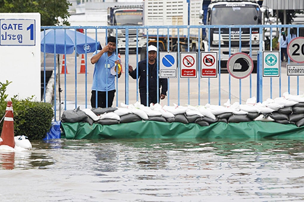 Workers look on behind flood protection barriers built at their factory at Amata Nakorn industrial Estate in Chonburi province, east of Bangkok, on Wednesday. Photo: Reuters