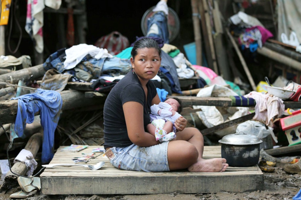 A mother holds her one-month-old daughter outside the remains of her damaged house in San Miguel town, Bulacan province. Photo: AP
