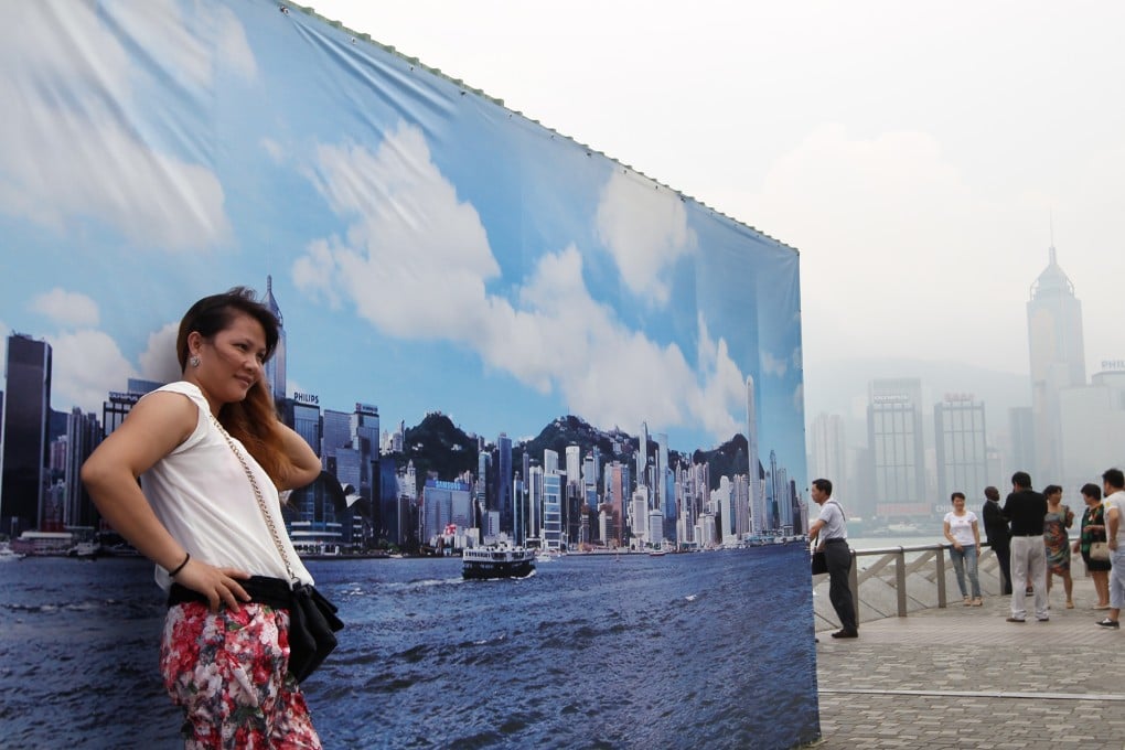 A tourist from mainland poses for photo in front of a large outdoor banner with an image of the Hong Kong island skyline at the waterfront in Tsim Sha Tsui. Photo: Sam Tsang