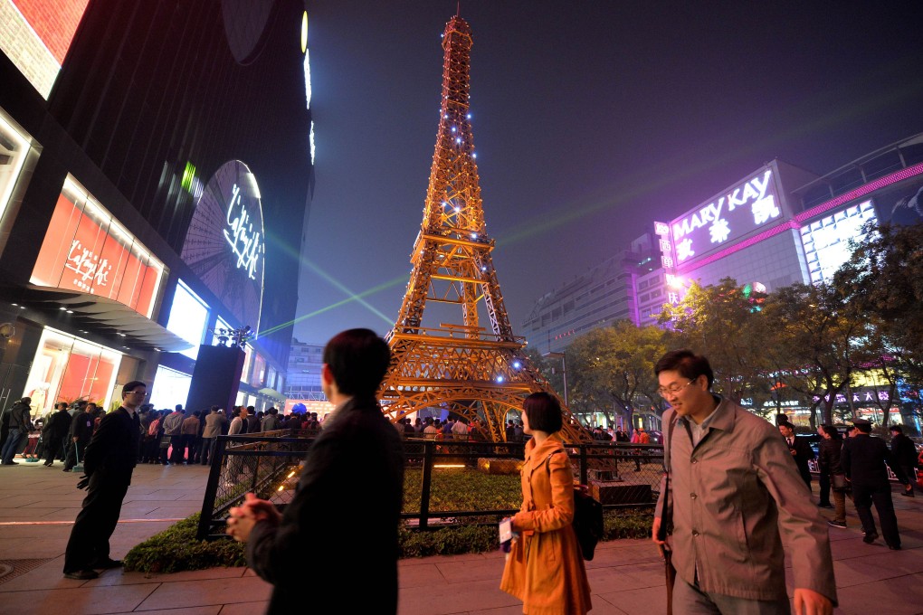 Chinese shoppers stand beside a model of the Eiffel Tower outside the Galeries Lafayette department store during its official opening in Beijing in October, 2013. Photo: AFP