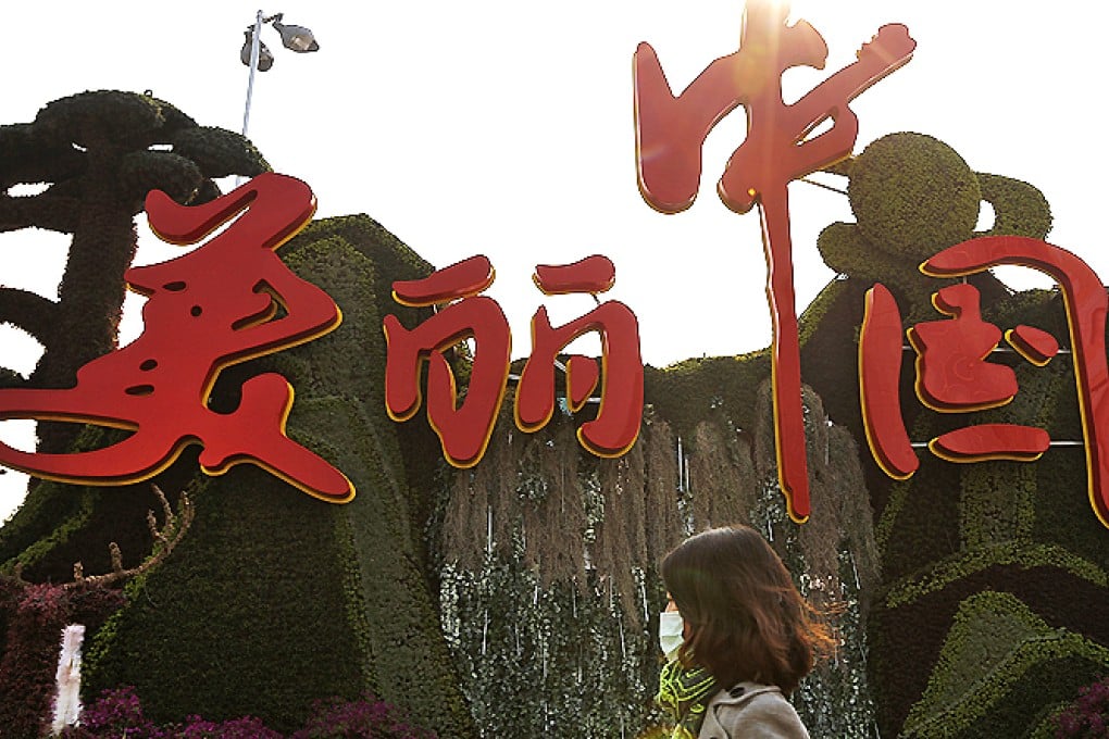 A woman wearing a mask walks past a decoration for the China National Tourism Campaign with a slogan 'Beautiful China' on display in Beijing on Monday. Photo: AP