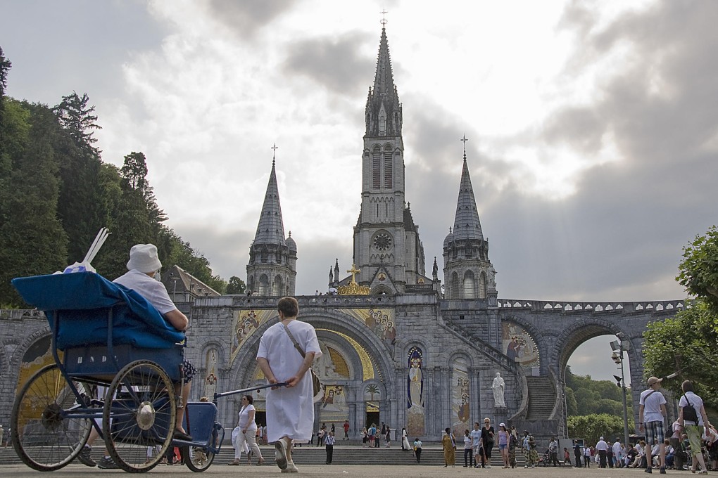 A hospitalier wheels a pilgrim towards the Rosary Basilica, in Lourdes.