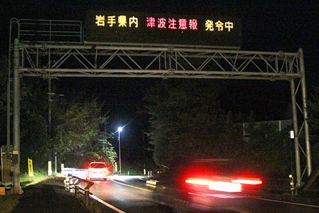 Cars pass under a neon tsunami warning following an earthquake off the coast of northeastern Japan early on Saturday. Photo: AP