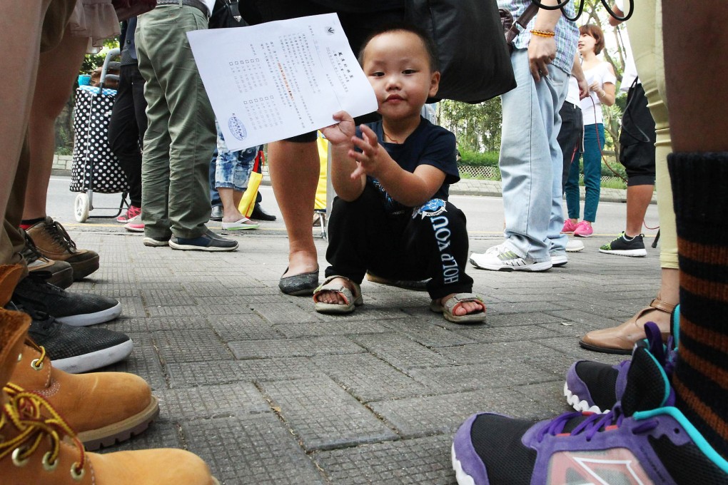 A young boy cheekily displays his application form as thousand of parents, most from the mainland, queue outside Fung Kai Kindergarten in Sheung Shui to try to secure places for next year. Photo: Felix Wong