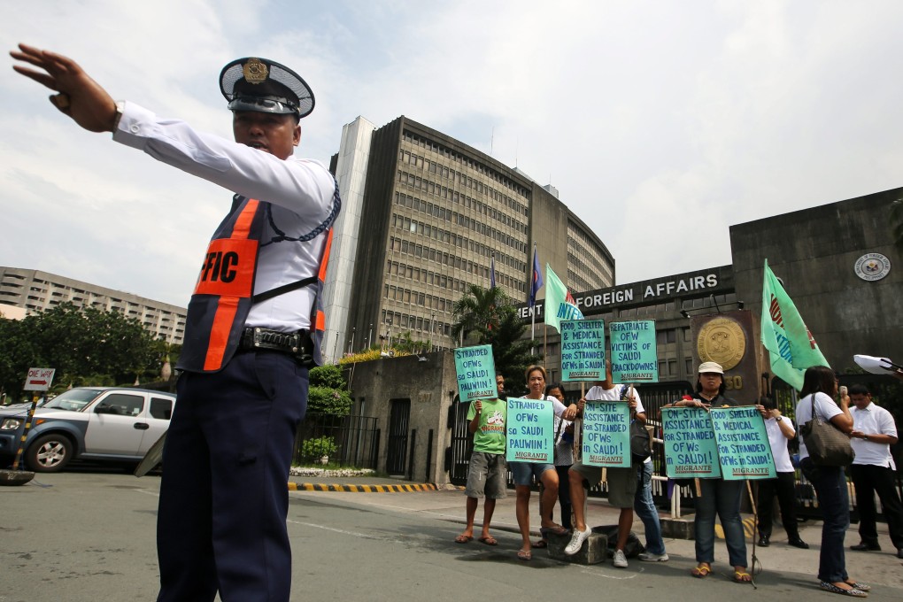 A Filipino security officer directs traffic as protesters hold banners outside the Department of Foreign Affairs. Photo: EPA