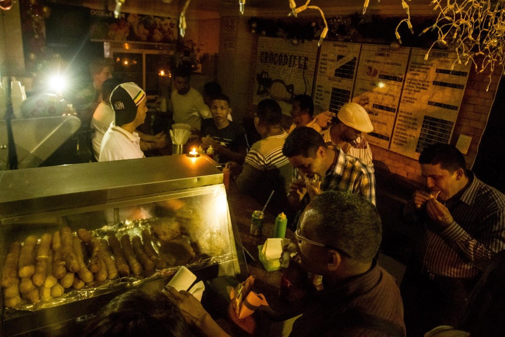 People at a food stall eat under the glow of candles and a TV camera's lights during the electricity blackout in Caracas. Photo: EPA