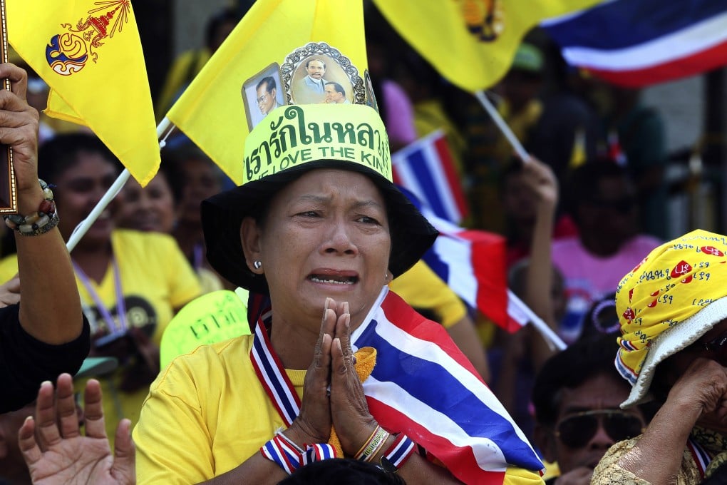 A Thai woman dressed in royal  yellow cries as she watches the king make a speech broadcast on a giant screen in Bangkok. Photo: AP