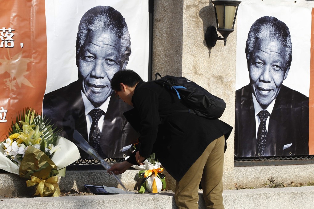 A Chinese man tributes flowers in front of a banner showing former South African president Nelson Mandela, at the Embassy of South Africa in Beijing. Photo: EPA