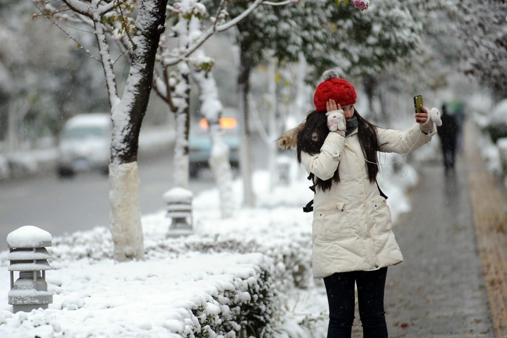 A woman takes a photograph of herself on a snow-covered pavement in Kunming. Photo: Xinhua
