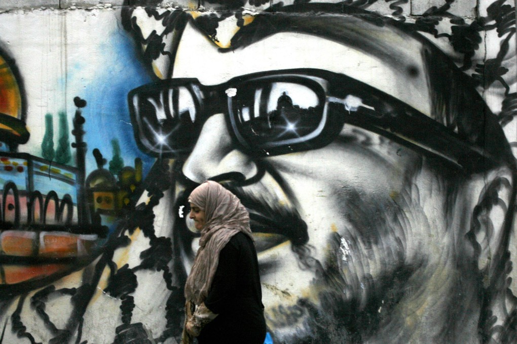 A woman walks past a graffiti of later Palestinian leader Yasser Arafat. Photo: AFP