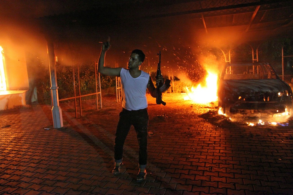 An armed man waving his rifle as buildings and cars are engulfed in flames after being set on fire inside the US consulate compound in Benghazi. Photo: AFP