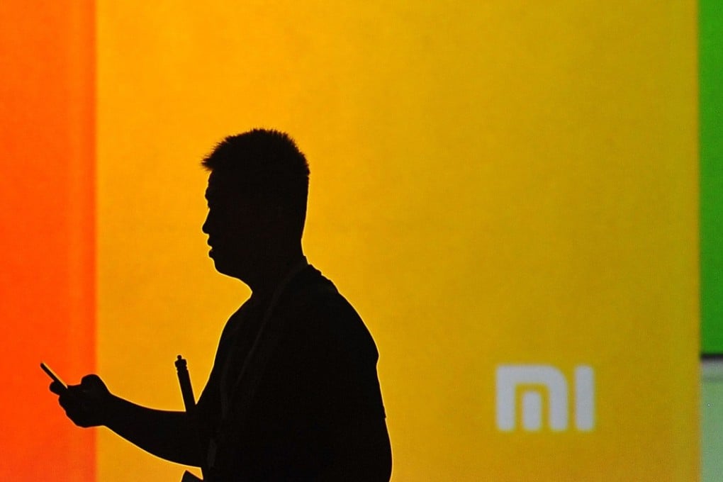 A man looks at his mobile phone as he walks past a screen during the launch of the new Xiaomi smartphone and Xiaomi TV in Beijing. Photo: AFP