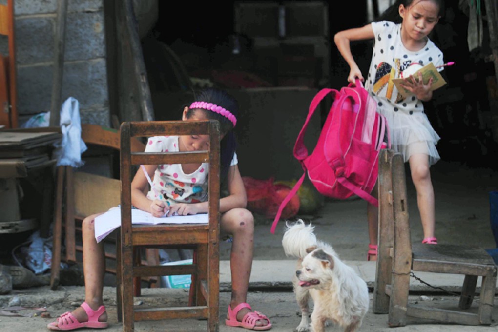 Two primary school girls are busy with schoolwork in front of their rundown settlement for migrant workers in Donghe village. Photo: Xinhua