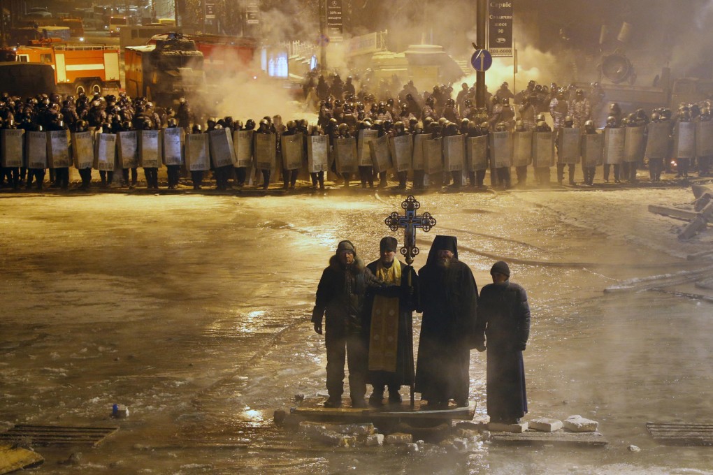 Orthodox priests pray standing between pro-European Union activists and police lines in Kiev. Photo: AP