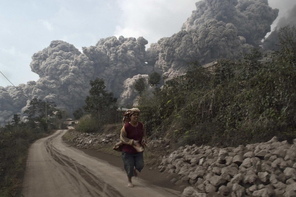 An Indonesian woman flees as Mount Sinabung, in western Sumatra, spews ash into the air, killing 16 people. Photo: Reuters