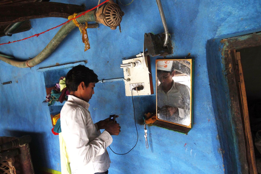 An Indian boy charges his mobile phone from an electric board powered by solar energy. Photo: Reuters