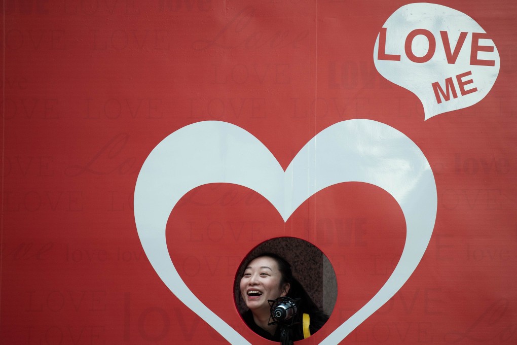 A woman smiles as she poses for a picture by a Valentine's Day cut-out displayed outside a shopping mall in Hong Kong on February 12, 2014. Photo: AFP