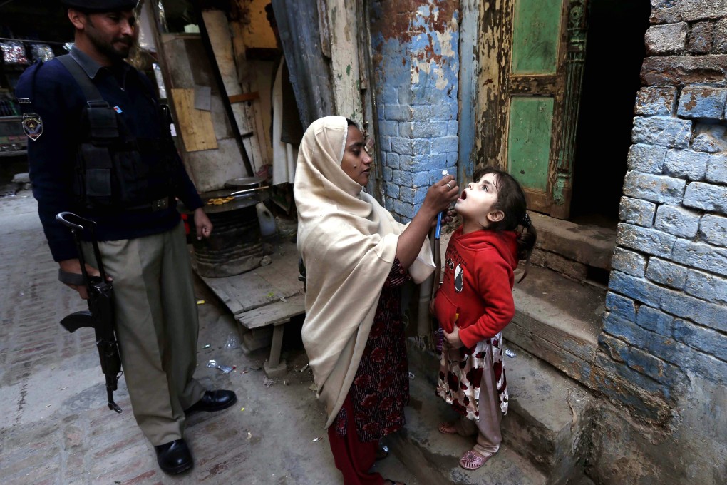 A health worker gives polio vaccines to a child in Peshawar with an armed policeman close by. A bomb has killed at least one policeman and wounded another during a vaccination campaign for polio. Photo: EPA