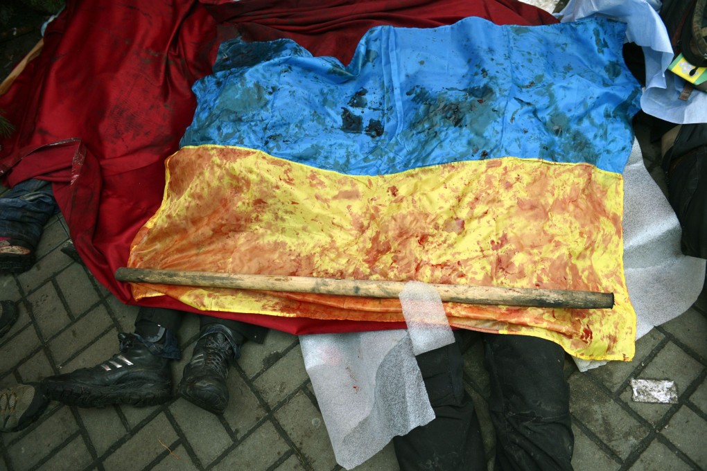 A bloody Ukranian flag covers the bodies of killed protesters in Kiev. Photo: EPA