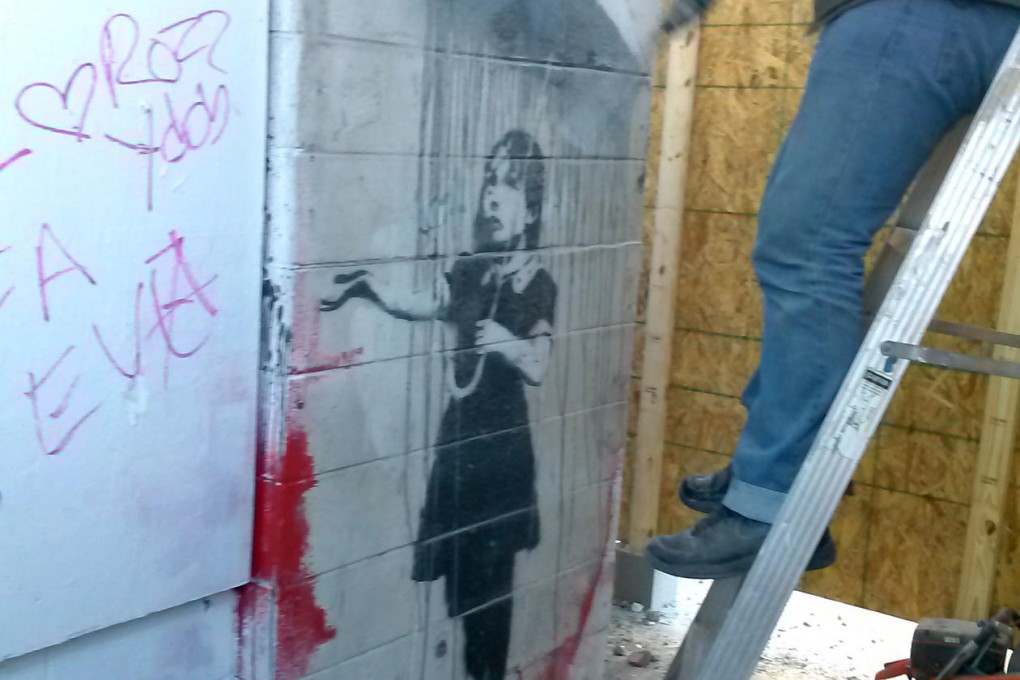 One of the two suspects cuts into the Banksy wall. Photo: AP