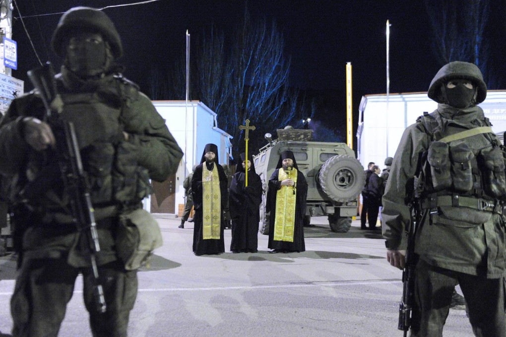Orthodox priests look on as Russian troops block access to Balaclava's border guard base. Photo: AFP