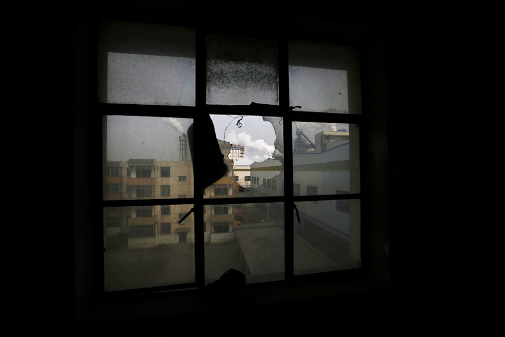 A steel mill seen through the broken window of an abandoned block of flats in Tangshan, Hebei. The province aims to slash 70 million tonnes of excess steel capacity by 2018. Photo: Reuters