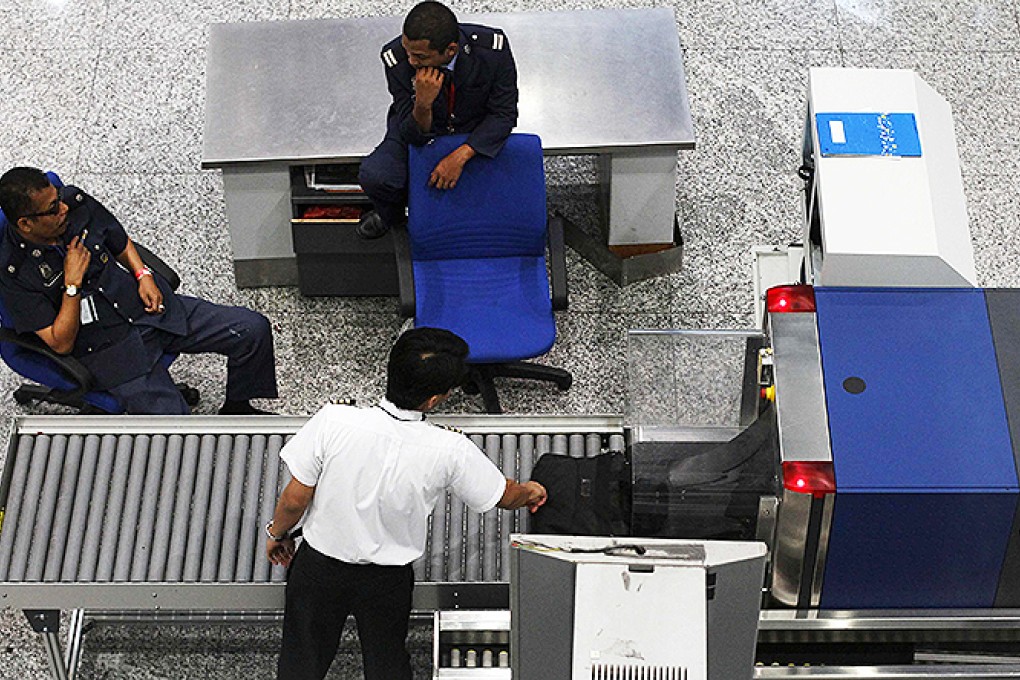 Airport security personnel chat as a pilot has his bag screened at the departure hall of the Kuala Lumpur International Airport in Sepang. Photo: Reuters
