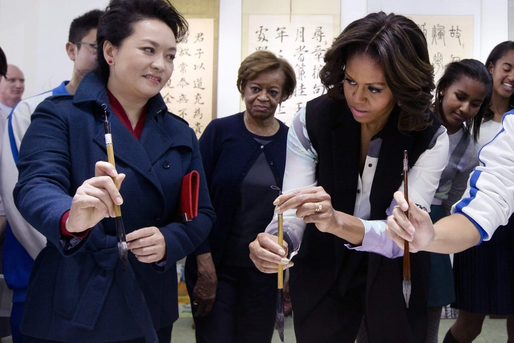 Peng Liyuan shows Michelle Obama how to hold a writing brush as they visit a Chinese traditional calligraphy class at the Beijing Normal School. Photo: Reuters