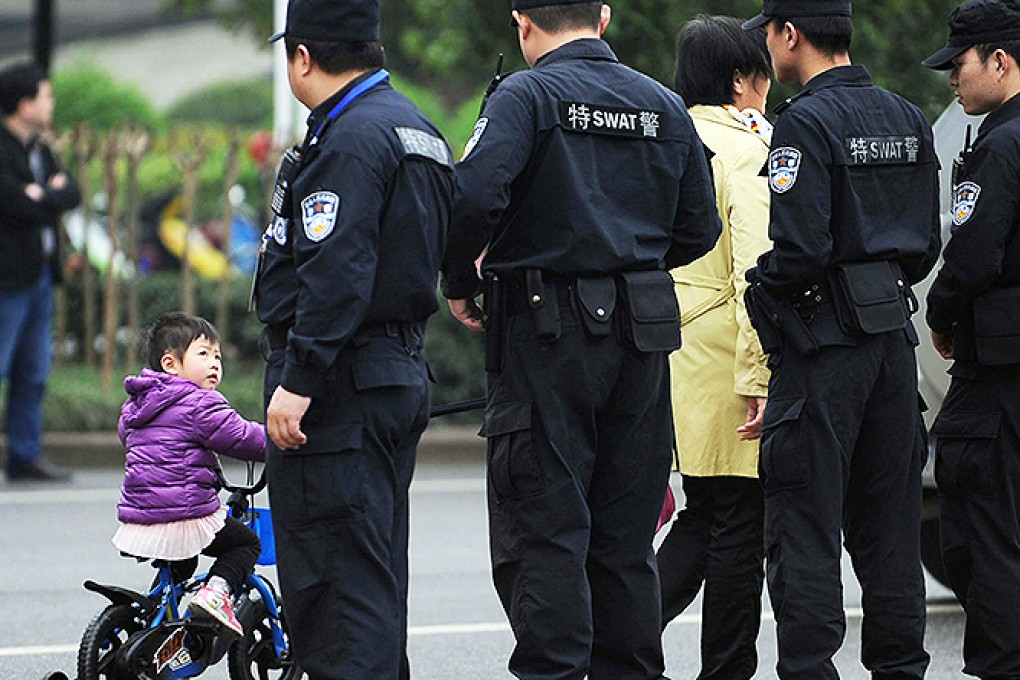 A young cyclist stares at police as they stand guard yesterday outside Xianning court, where mining tycoon Liu Han went on trial. Photo: AFP