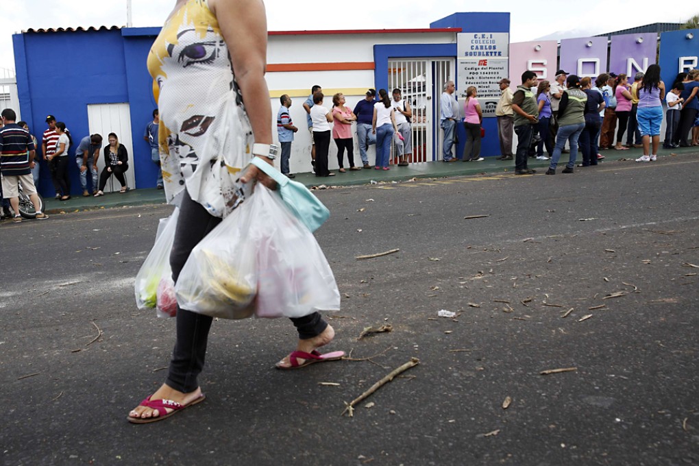 A woman carrying bags of groceries walks past a line of people queuing up to buy food at a supermarket in San Cristobal, Venezuela. Photo: Reuters