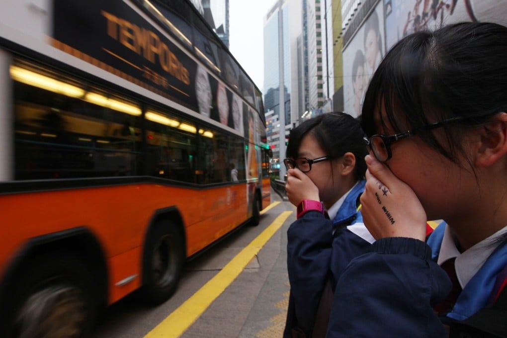 Students cover their noses to avoid emissions from vehicles as they cross Yee Wo Street in Causeway Bay. Photo: Nora Tam
